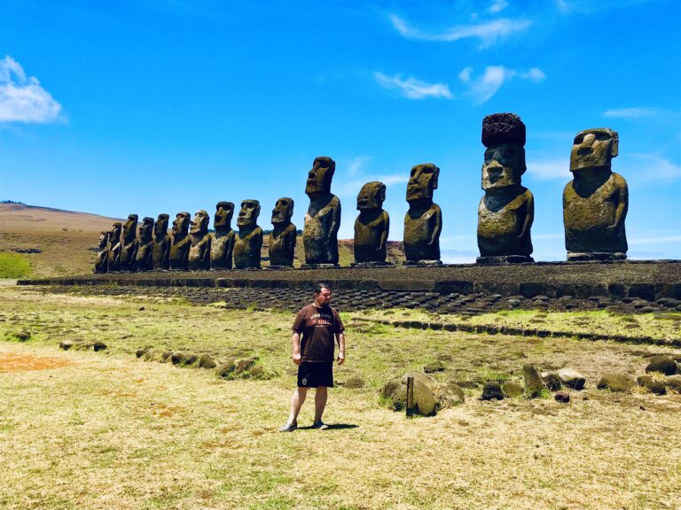 Mężczyzna stojący na tle gigantycznej platformy Ahu Tongariki z 15 posągami moai na Wyspie Wielkanocnej.
