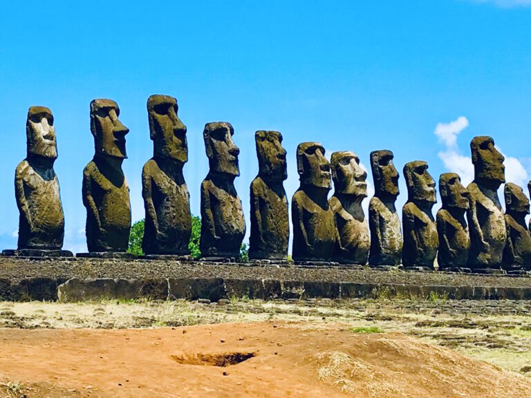 Rząd piętnastu majestatycznych posągów moai ustawionych na platformie Ahu Tongariki, widok z boku na tle błękitnego nieba.