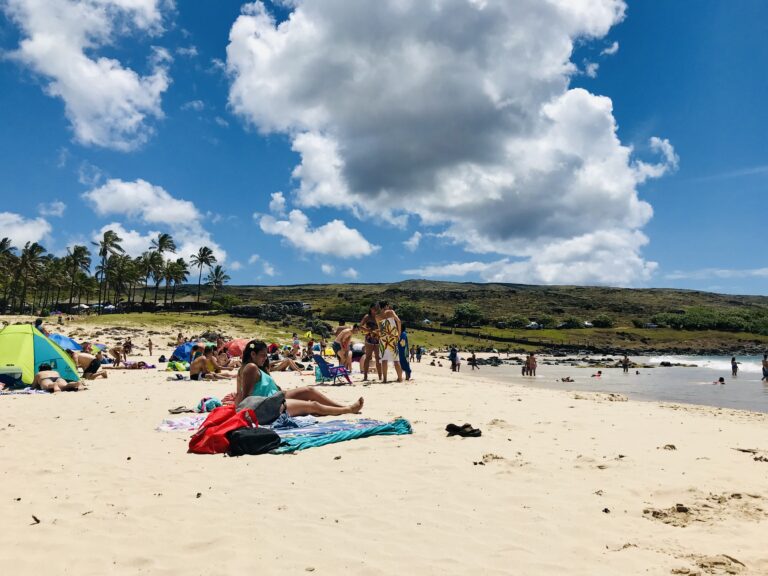 Tętniąca życiem piaszczysta plaża Anakena z wypoczywającymi ludźmi, palmami w tle i turkusową wodą oceanu.