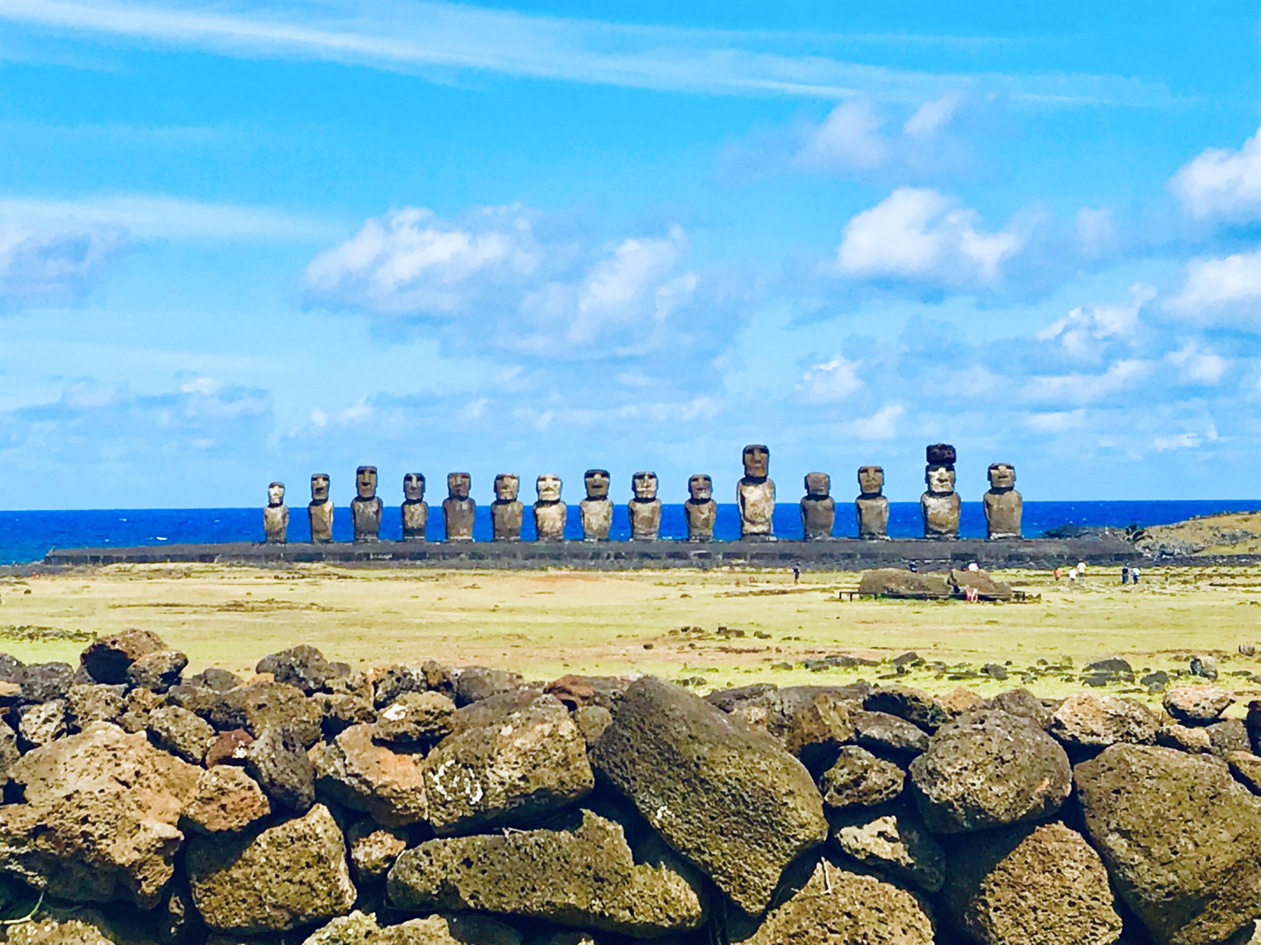 Panorama piętnastu posągów moai na platformie Ahu Tongariki, widziana zza tradycyjnego muru z ułożonych wulkanicznych kamieni.