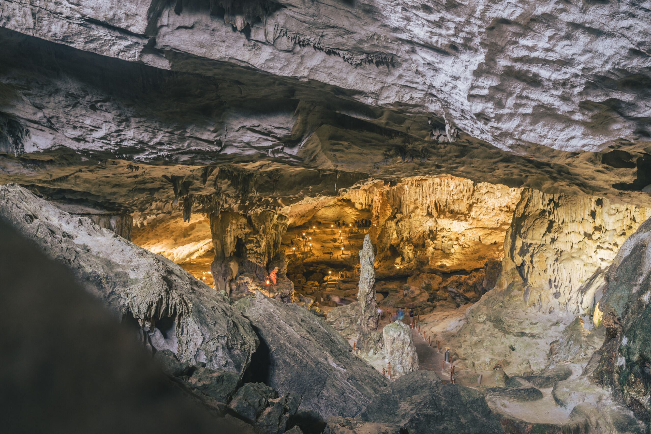 Szerokie ujęcie wnętrza ogromnej jaskini z podświetlonymi formacjami skalnymi, stalaktytami i stalagmitami oraz wyznaczoną ścieżką dla zwiedzających.