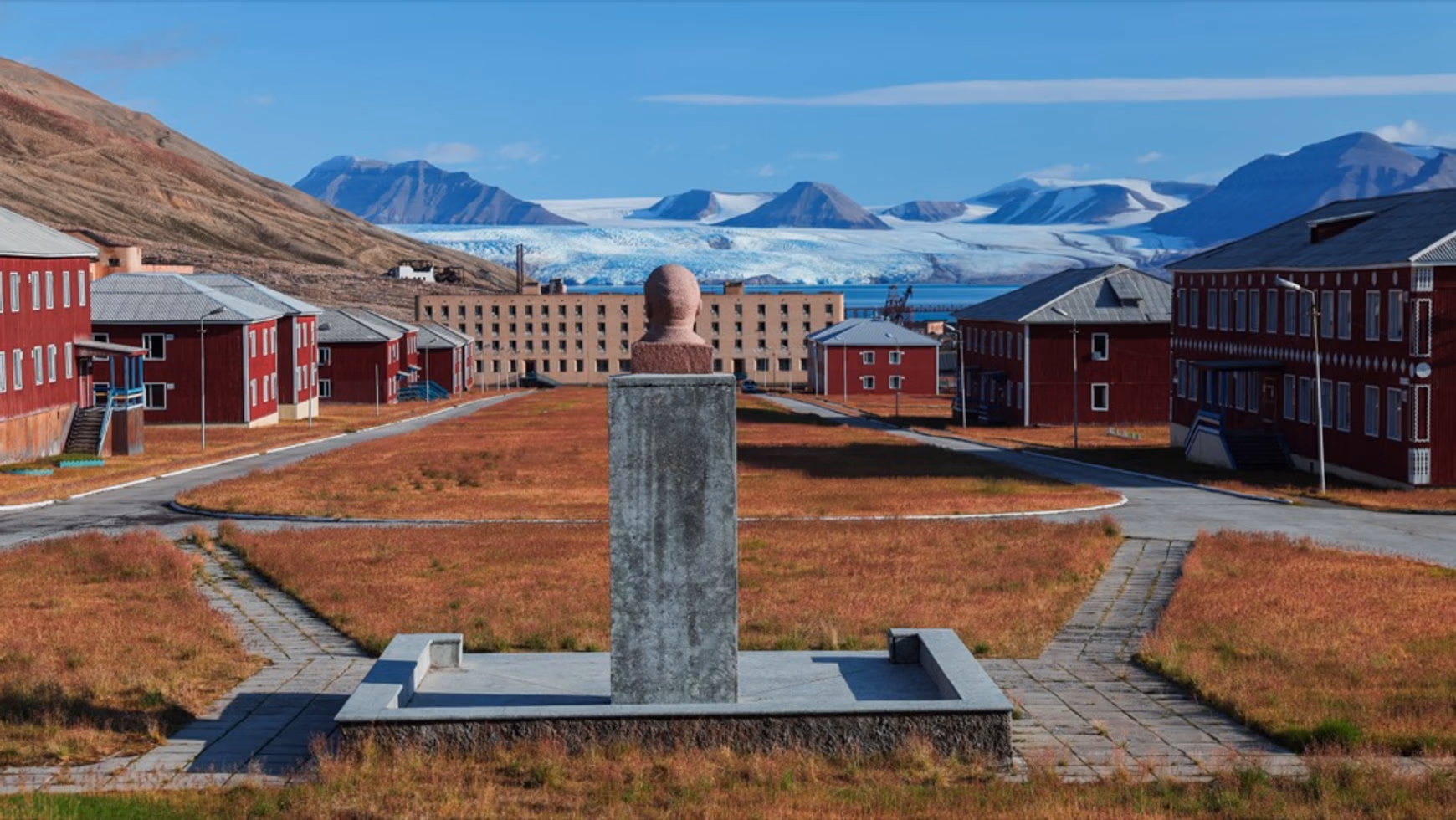 Popiersie Lenina na wysokim postumencie w centrum opuszczonej radzieckiej osady górniczej Pyramiden, z lodowcem i górami w tle.